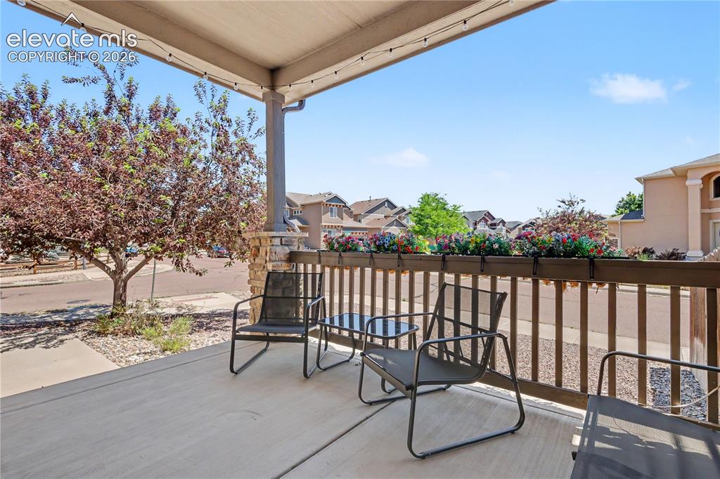 6598 Alliance Loop Colorado Springs, CO 80925 - Photo 35 of 39 Covered porch featuring concrete flooring, a stone-wrapped column, and a wooden railing with attached planter boxes