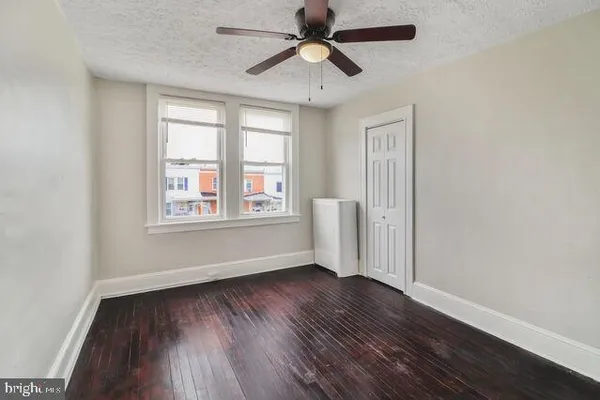 an empty room with wooden floor chandelier fan and windows