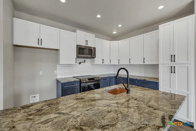 a kitchen with kitchen island granite countertop a stove sink and cabinets