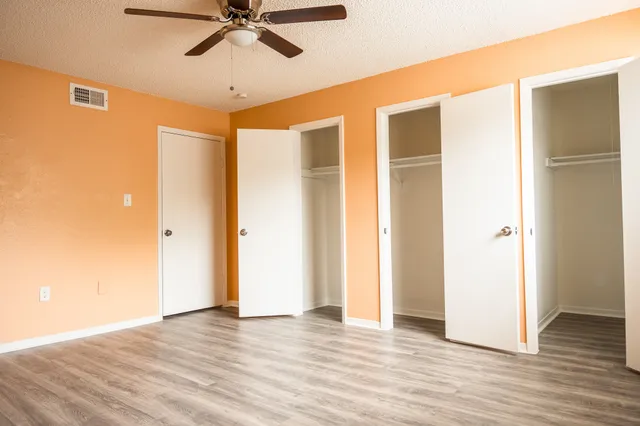 a view of an empty room with wooden floor and a ceiling fan