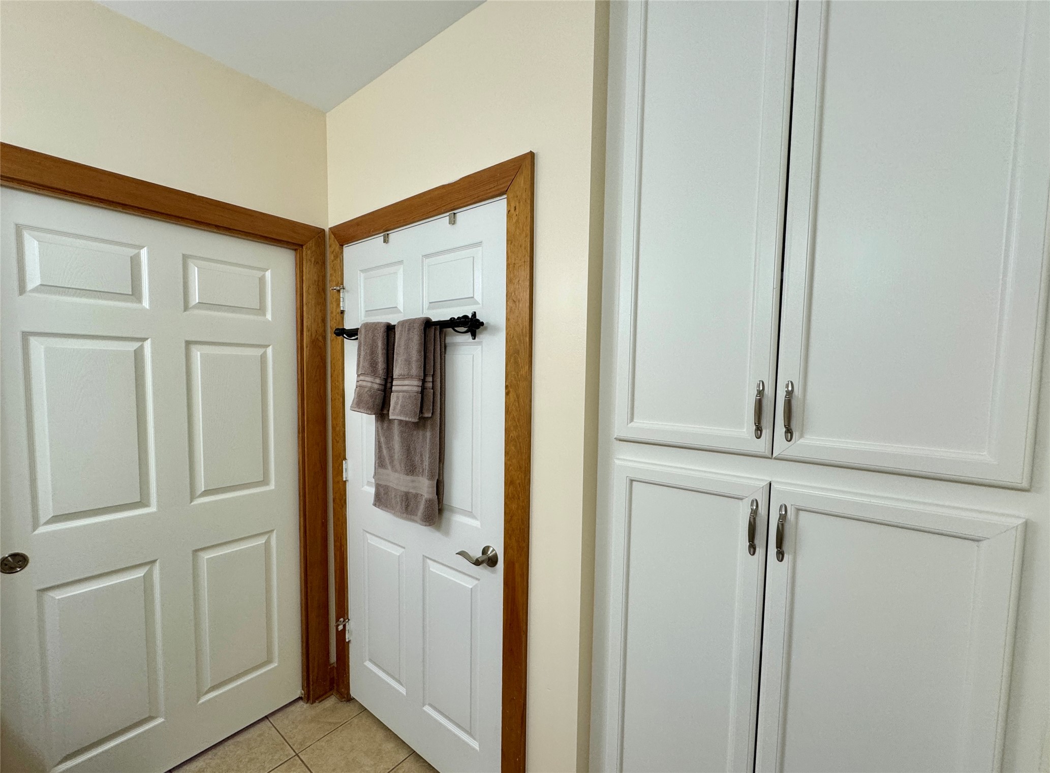 55 Lake Road Huntsville, TX 77320 - Photo 30 of 50 This photo of the guest bath shows a clean, well-lit space with white paneled doors and cabinetry, accented by wood trim. There are two doors, one with hanging towels, and more storage with large cabinets. The floor is tiled, giving a neat and organized appearance.