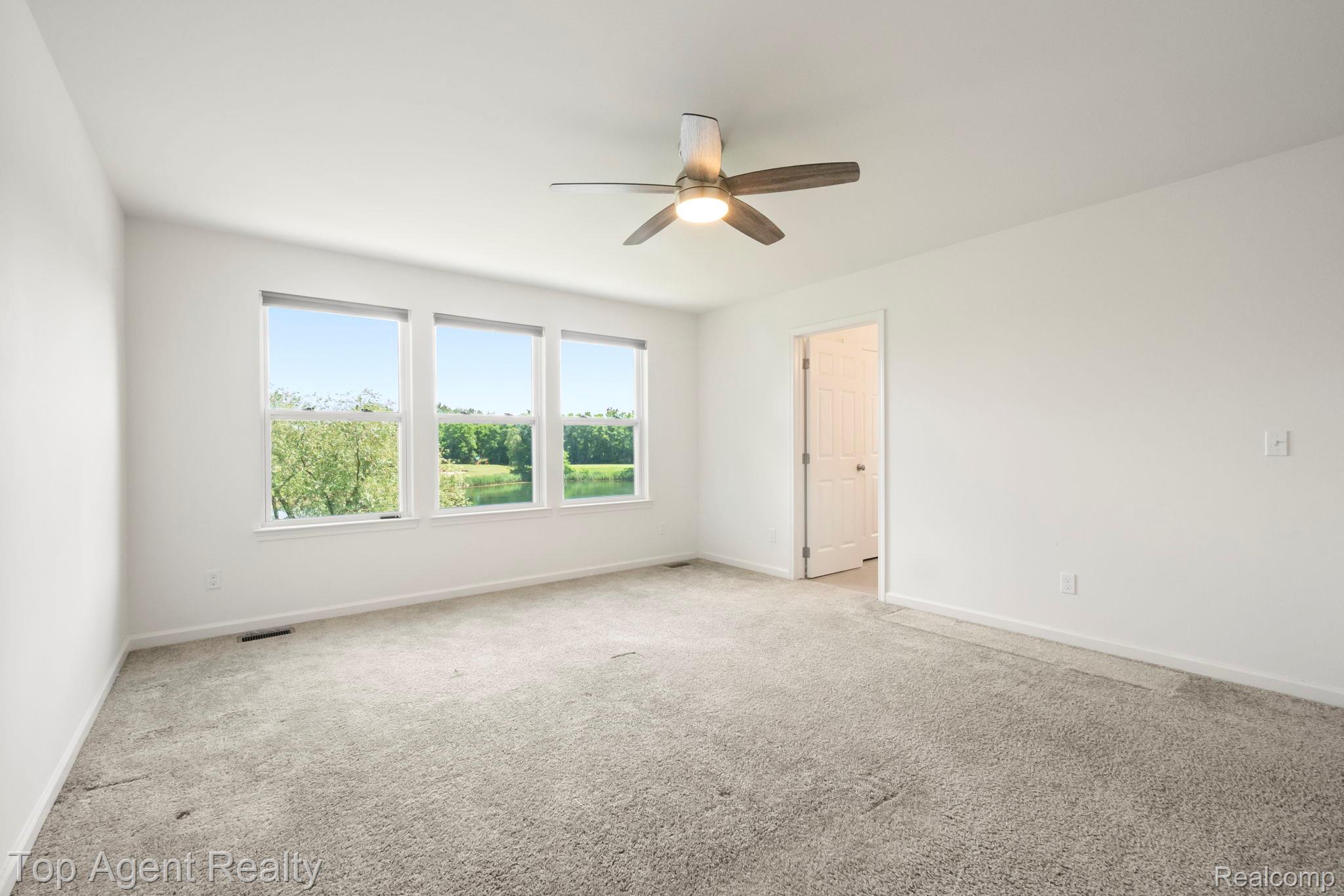 63770 Dequindre Road Washington, MI 48095 - Photo 4 of 61 Spacious room featuring three large windows, light gray carpet, white walls, a ceiling fan with integrated lighting, and a white interior door
