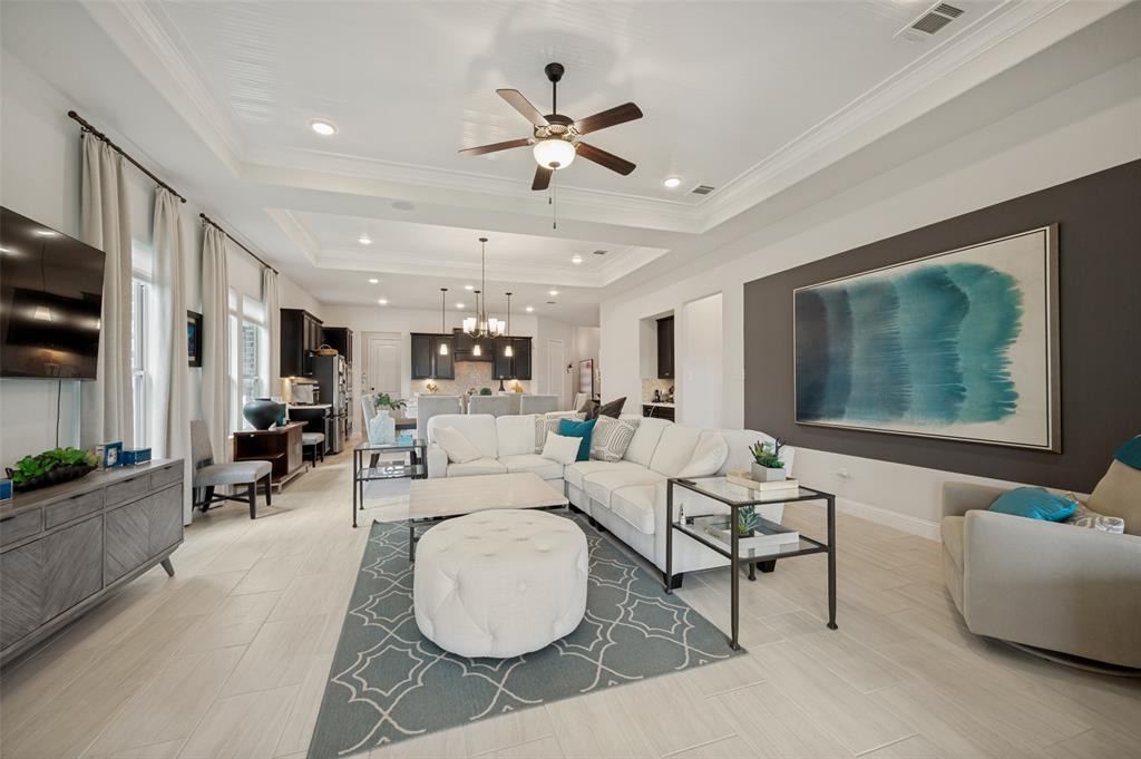 7821 Kentmere The Colony, TX 75056 - Photo 12 of 40 The expansive living room impresses with sleek tile flooring, an elegant tray ceiling, and walls of windows that flood the space with natural light. A striking designer accent wall creates a sophisticated focal point, while the open-concept layout offers seamless flow for comfortable everyday living and effortless entertaining.