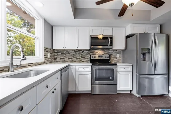 a kitchen with stainless steel appliances white cabinets a sink a window and a refrigerator