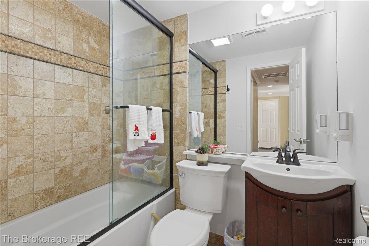 261 Reymont Road Waterford, MI 48327 - Photo 18 of 49 Bathroom featuring a tile-surround bathtub with a glass shower enclosure, a curved vanity with a basin sink, and a large wall-mounted mirror with overhead lighting