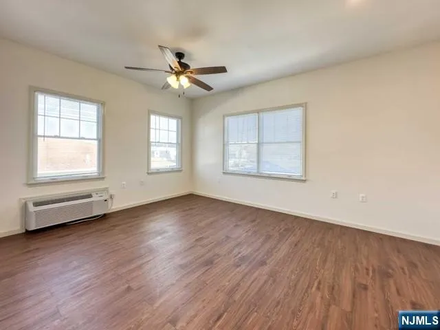 an empty room with wooden floor ceiling fan and windows