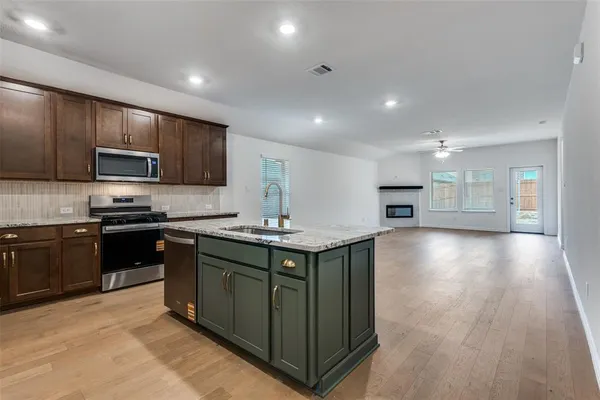 a kitchen with stainless steel appliances granite countertop a sink a stove top oven a refrigerator with wooden floors