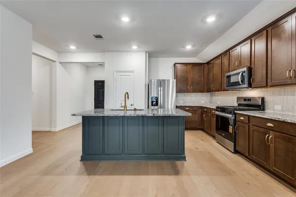 a kitchen with stainless steel appliances granite countertop a sink a stove a refrigerator cabinets and a kitchen island