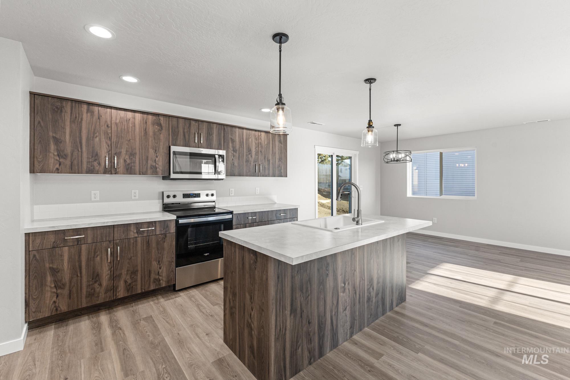 1436 Long Pond Street Middleton, ID 83644 - Photo 4 of 24 Kitchen featuring dark brown cabinets, appliances with stainless steel finishes, light countertops, a center island with sink, and hanging light fixtures