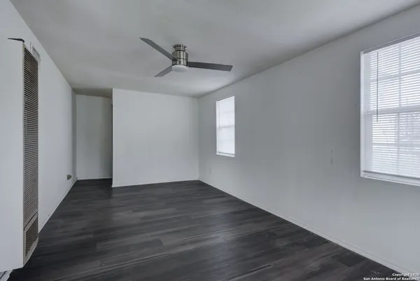 an empty room with wooden floor fan and windows