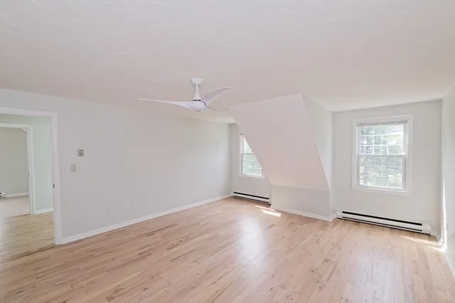 an empty room with wooden floor fan and windows