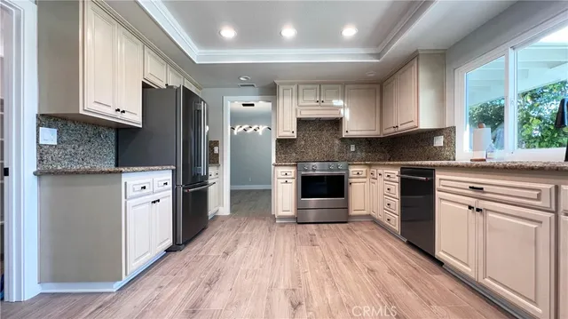a large kitchen with stainless steel appliances granite countertop a stove a sink and white cabinets with wooden floor