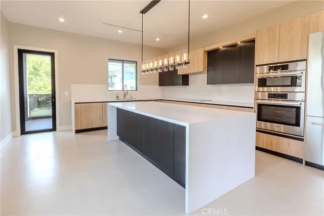 a large kitchen with stainless steel appliances a large counter top a stove a sink and a refrigerator