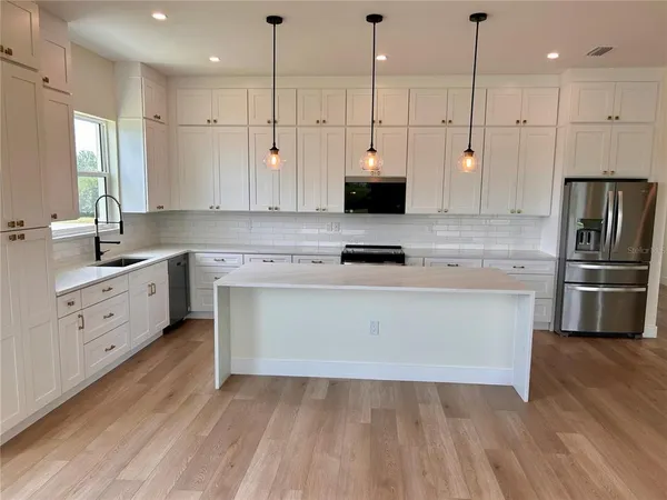 a kitchen with stainless steel appliances white cabinets a sink a stove a refrigerator and a window