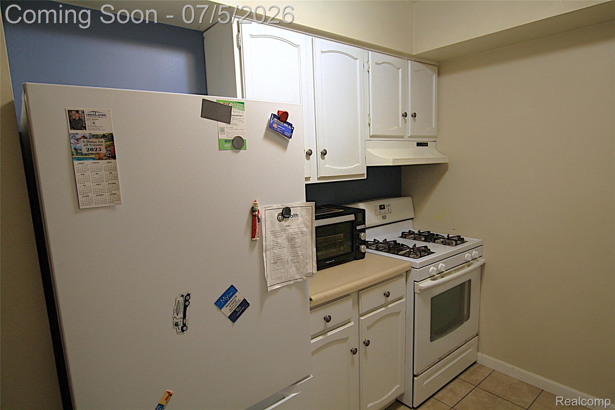 12403 Willard Road Montrose, MI 48457 - Photo 13 of 30 Kitchen with white cabinets, white appliances, light tile patterned flooring, light countertops, and under cabinet range hood