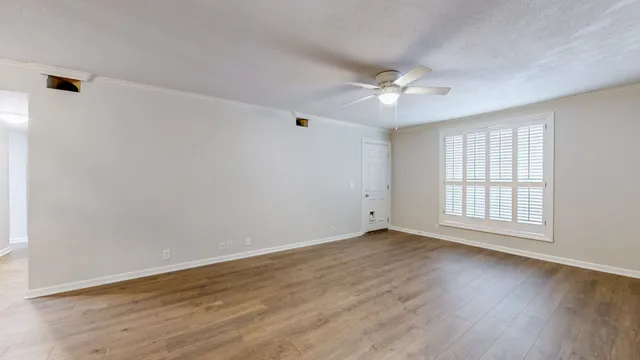 an empty room with wooden floor ceiling fan and windows