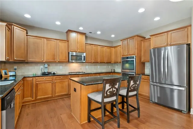 a kitchen with stainless steel appliances granite countertop a refrigerator a sink dishwasher a stove and white cabinets with wooden floor