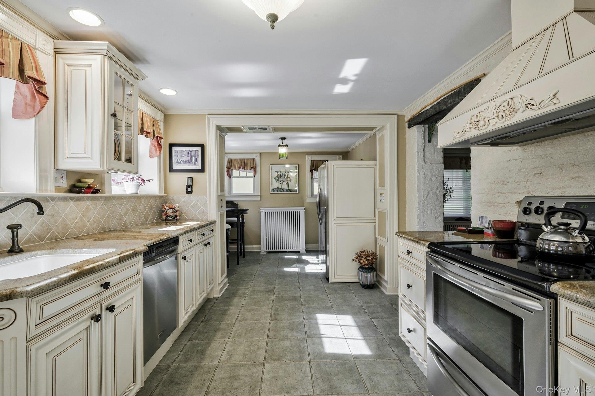 126 Cove Road Oyster Bay, NY 11771 - Photo 13 of 42 Kitchen with decorative backsplash, stainless steel appliances, premium range hood, light stone countertops, and radiator heating unit