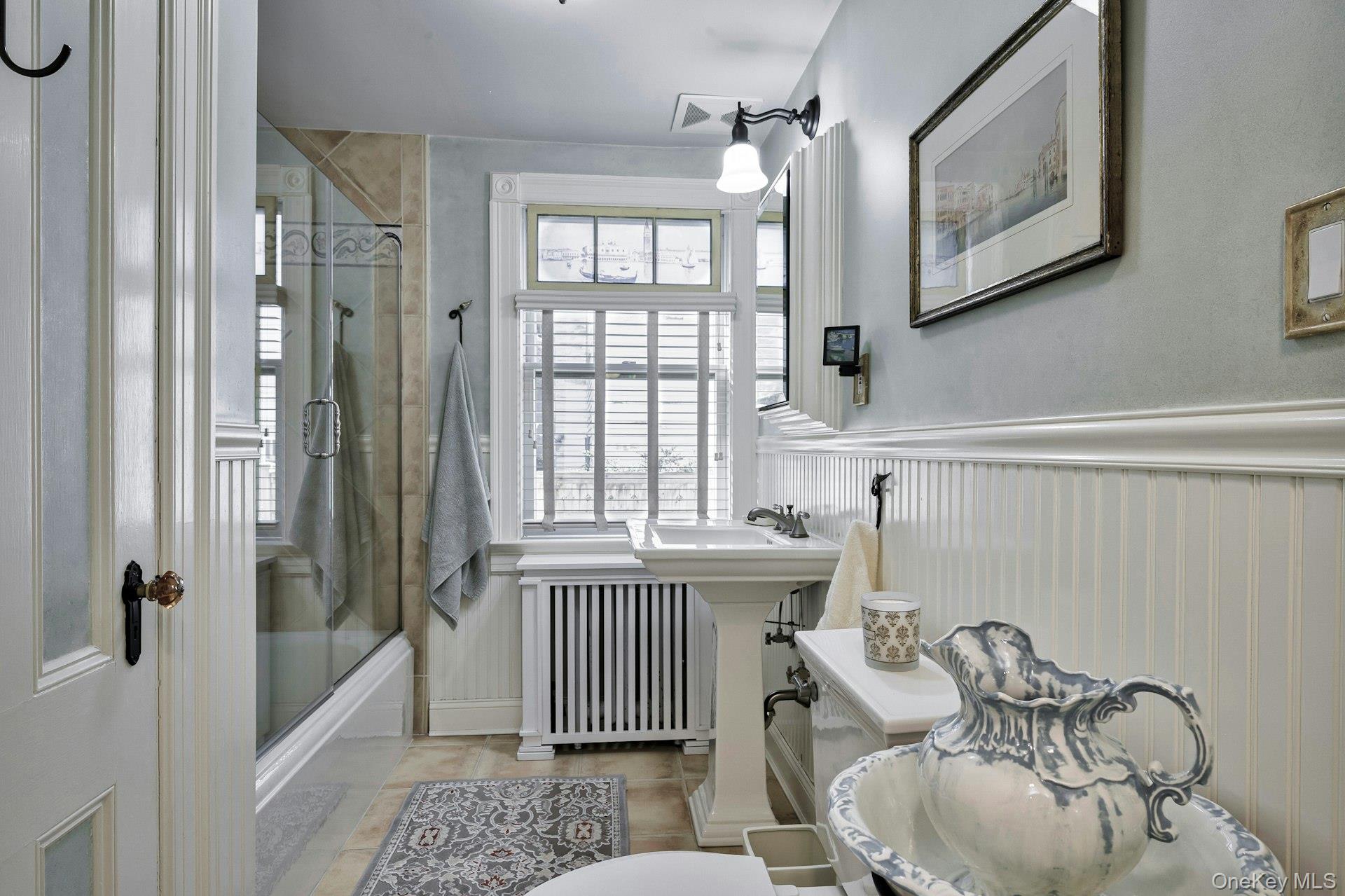 126 Cove Road Oyster Bay, NY 11771 - Photo 29 of 42 Bathroom featuring radiator, bath / shower combo with glass door, and a wainscoted wall