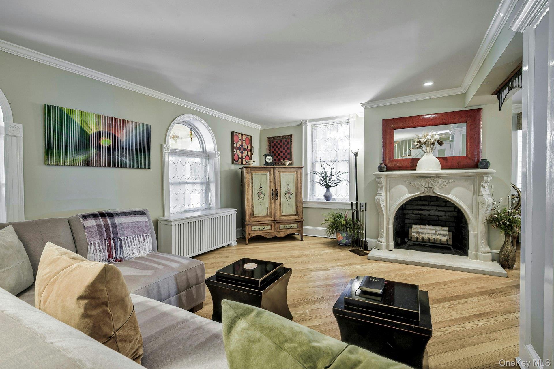 126 Cove Road Oyster Bay, NY 11771 - Photo 10 of 46 Living room featuring wood finished floors, crown molding, a fireplace with raised hearth, and radiator heating unit