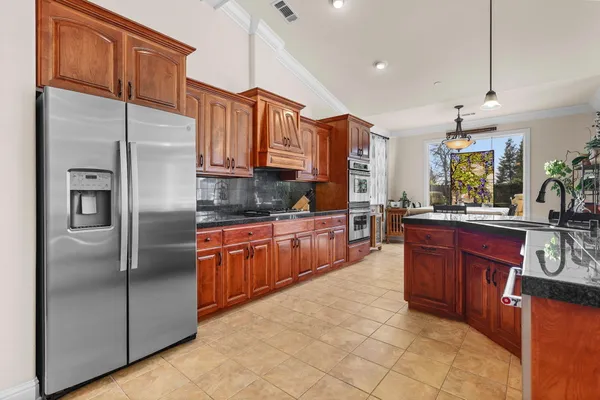 a kitchen with stainless steel appliances kitchen island granite countertop a refrigerator a stove a sink a dining table and chairs with wooden floor