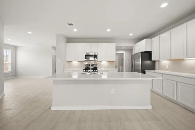 a view of kitchen with stainless steel appliances granite countertop a stove a sink a refrigerator and white cabinets with wooden floor