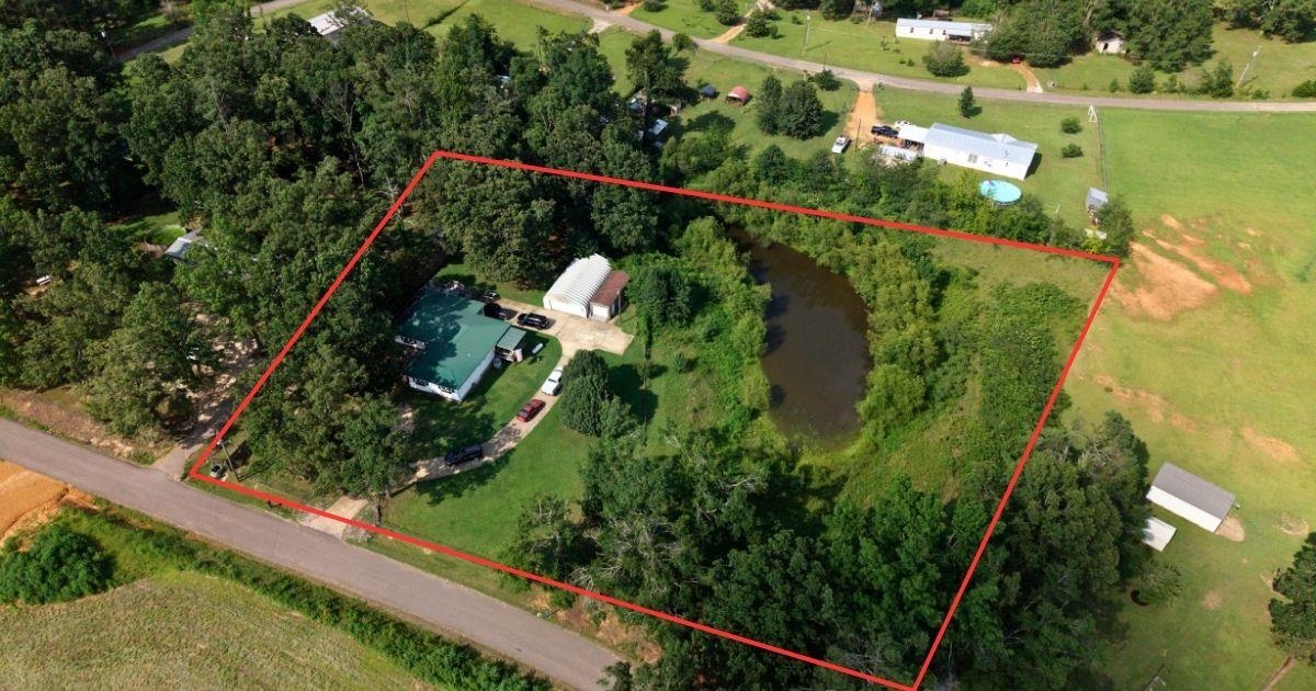 772 Rushing Road Michie, TN 38357 - Photo 16 of 19 Aerial property view featuring a main residence, an accessory building, a private pond, mature trees, and an expansive grassy area