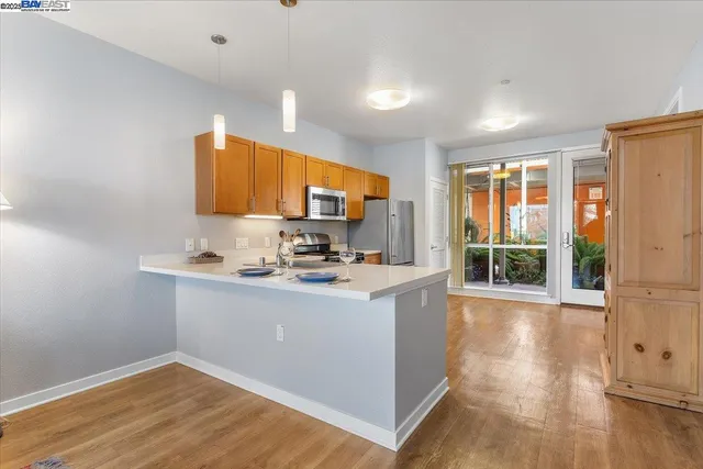 a view of kitchen with stainless steel appliances granite countertop a stove top oven a sink with wooden cabinets and wooden floor