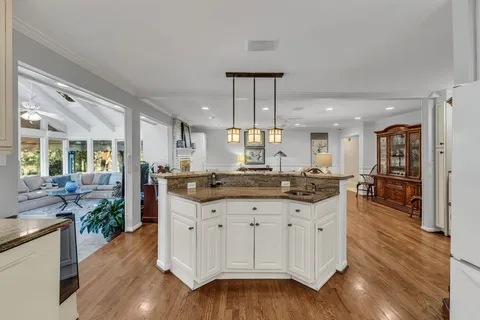 a kitchen with stainless steel appliances granite countertop a stove a sink a refrigerator and white cabinets with wooden floor