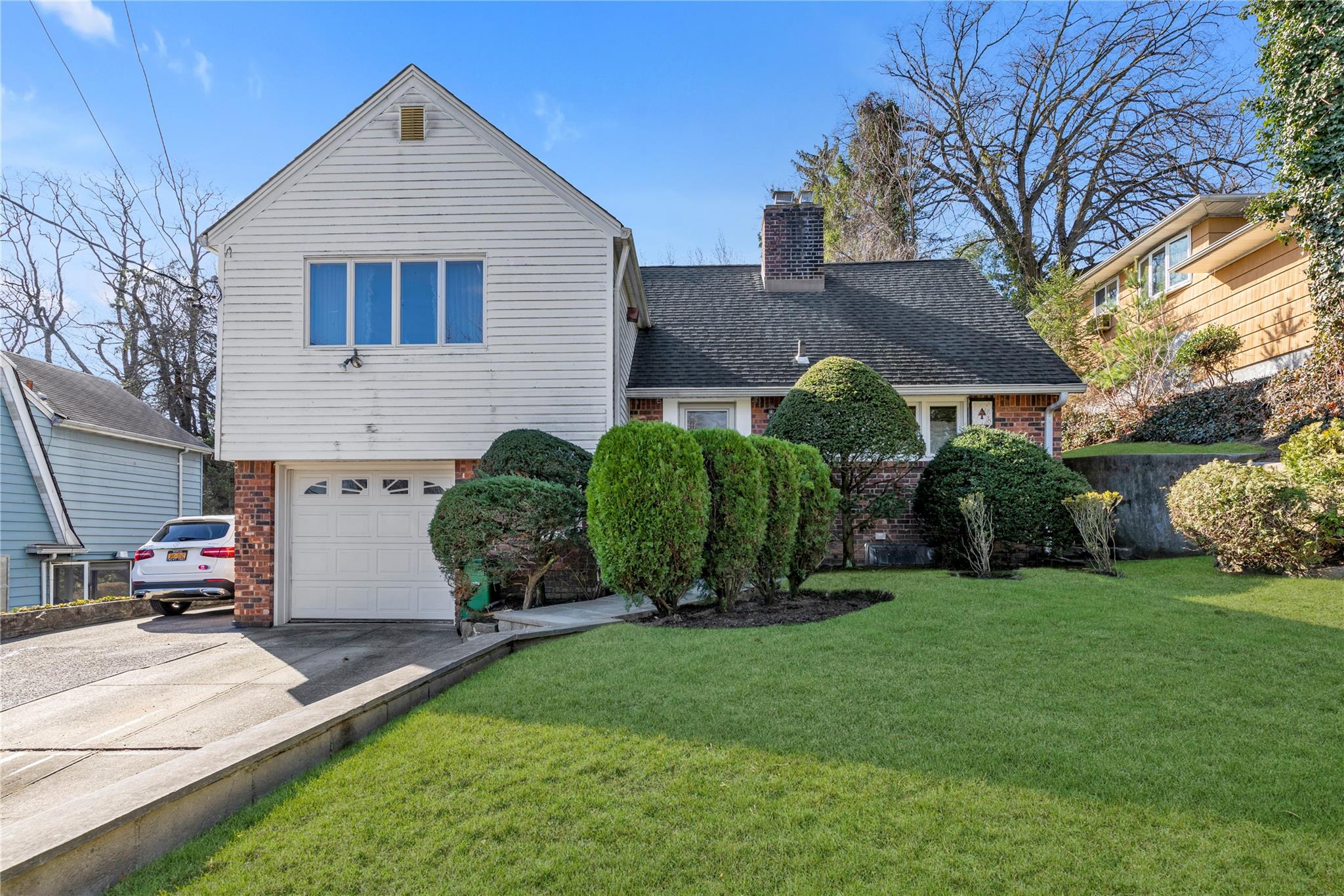 350 Arleigh Road Queens, NY 11363 - Photo 1 of 1 View of front of house with a chimney, driveway, brick siding, a garage, and a shingled roof