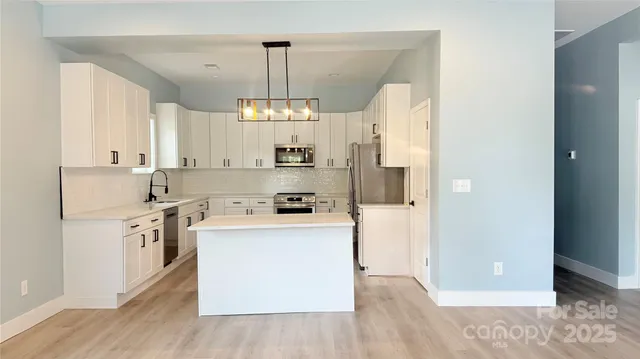 a kitchen with stainless steel appliances a refrigerator a stove a sink dishwasher and white cabinets with wooden floor