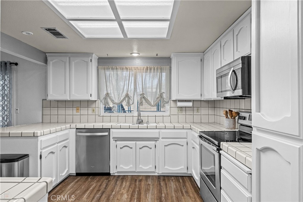 3585 Cabrillo Court Merced, CA 95348 - Photo 11 of 42 a kitchen with a sink dishwasher stove and white cabinets with wooden floor