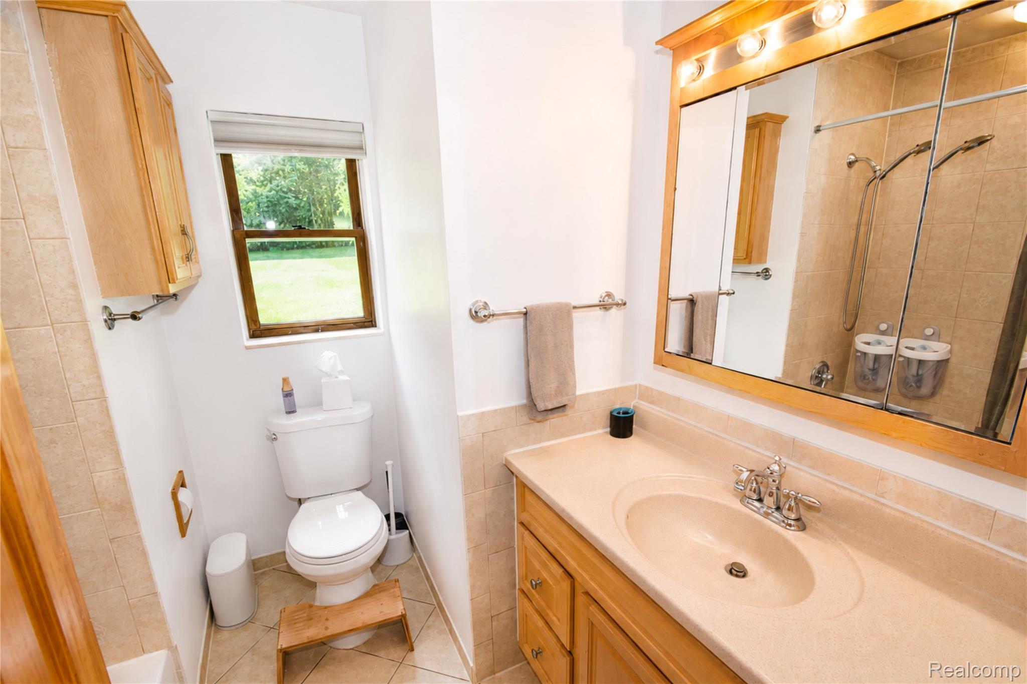1405 Middle Road Highland, MI 48357 - Photo 11 of 18 Bathroom featuring a wood-finish vanity with an integrated sink, a large mirrored medicine cabinet with overhead lighting, a window with exterior views, and a tiled shower enclosure