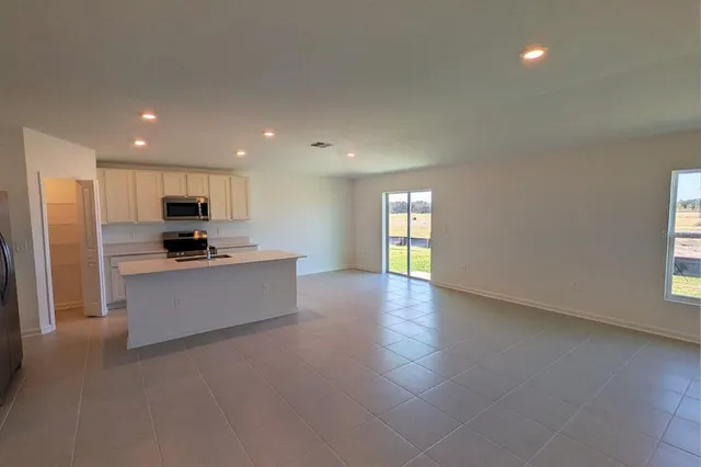 a large kitchen with stainless steel appliances granite countertop a stove a sink a refrigerator and white cabinets with wooden floor