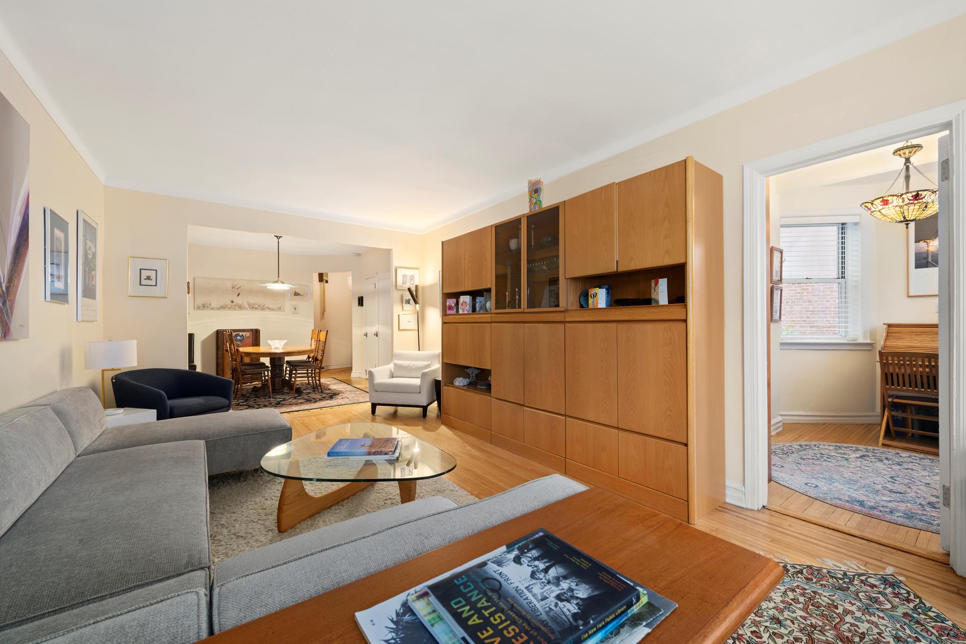 86-10 34th Avenue, Unit 113 Queens, NY 11372 - Photo 5 of 13 a living room with furniture a refrigerator and a dining table with wooden floor