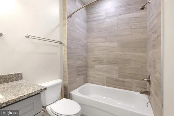 a bathroom with a granite countertop bathtub shower sink vanity and toilet