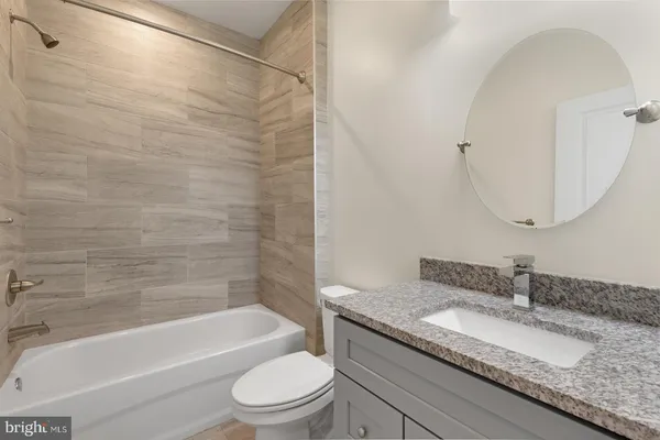 a bathroom with a granite countertop bathtub shower sink vanity mirror and toilet