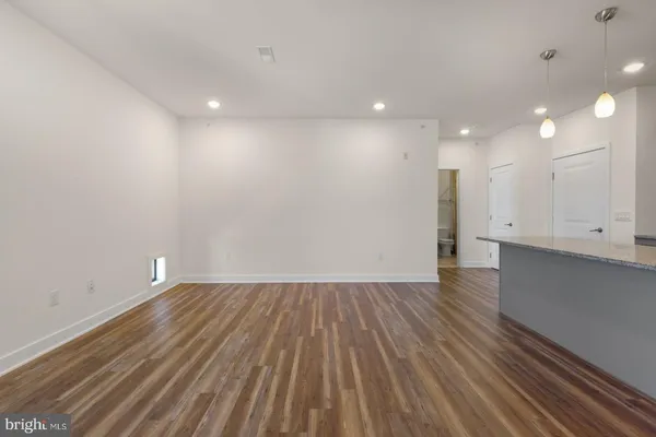 a view of an empty room with wooden floor and kitchen