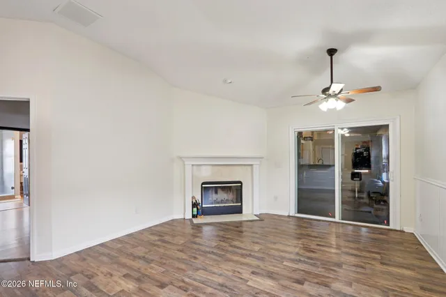 a view of an empty room with wooden floor fireplace and a window
