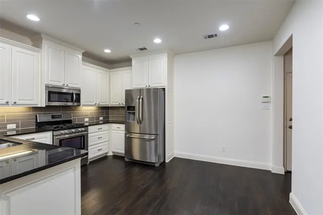 a kitchen with stainless steel appliances granite countertop a refrigerator a stove top oven a sink and dishwasher with wooden floor