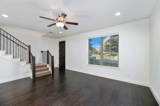 a view of an empty room with wooden floor and a ceiling fan