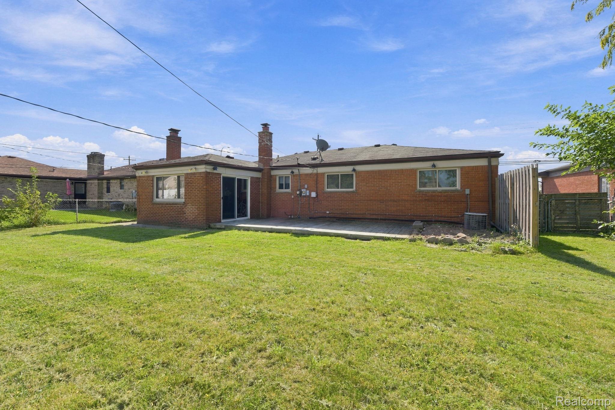 13265 12 Mile Road Warren, MI 48088 - Photo 33 of 33 Expansive green lawn, brick exterior, two brick chimneys, sliding glass door, and a paved patio area