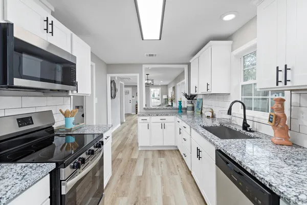 a kitchen with stainless steel appliances granite countertop a stove top oven a sink dishwasher and a microwave with wooden floor