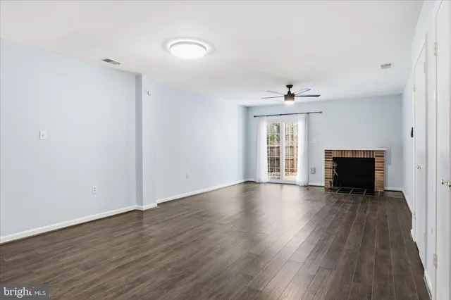 a view of an empty room with wooden floor fireplace and a window