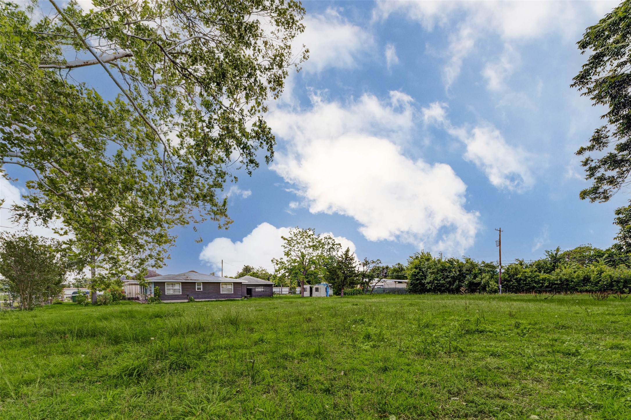 8537 Rannie Road Houston, TX 77080 - Photo 5 of 15 Wide side-lot perspective emphasizing the open land area, mature tree canopy, and natural spacing around the existing improvements. The home is secondary to the lot, while the surrounding yard, fencing, and detached structure help show the property’s practical utility. This view is ideal for buyers considering parking, storage, contractor use, builder staging, or long-term land planning.