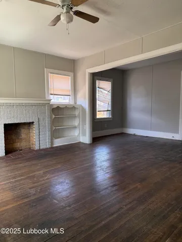 an empty room with wooden floor fireplace and windows
