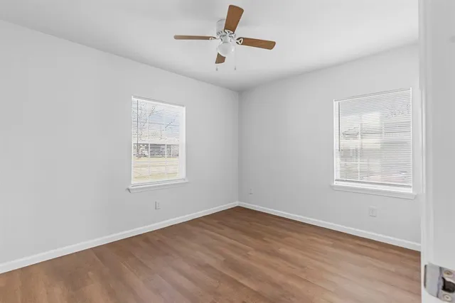 an empty room with wooden floor ceiling fan and windows
