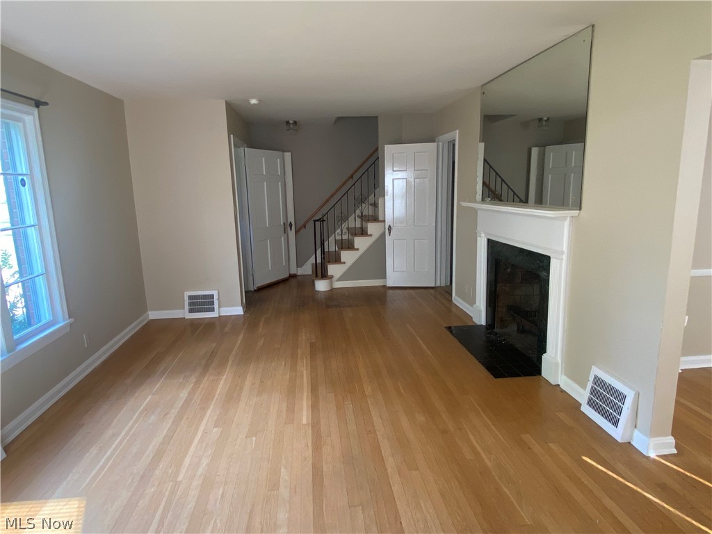 Hardwood flooring, white window trim, white fireplace mantel, black fireplace surround, and a staircase with a black handrail