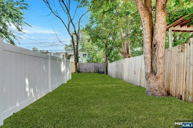 a view of a backyard with large trees and wooden fence