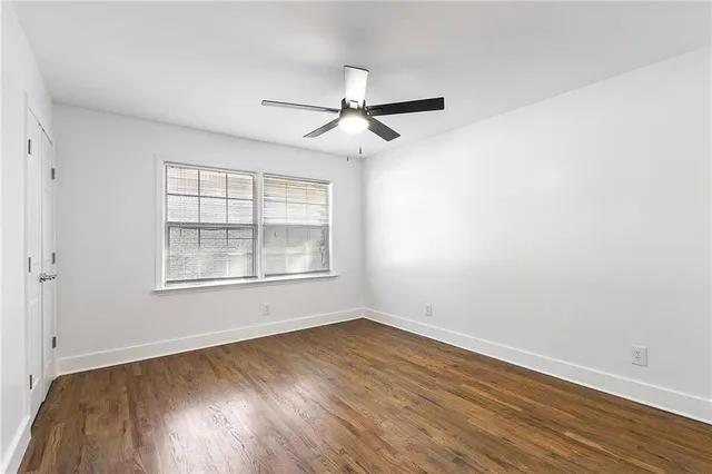 an empty room with wooden floor ceiling fan and windows